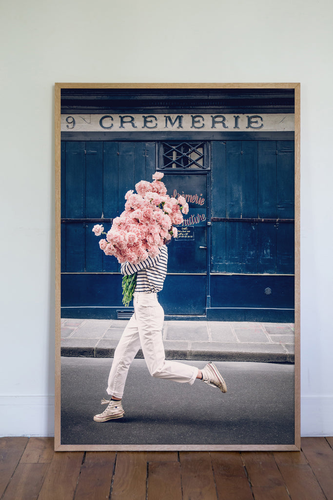 Follow Your Bliss is an image of a girl with a huge bouquet of pink carnations in her arms skipping along the street in front of La Crèmerie in the 6th Arrondissement in Paris.