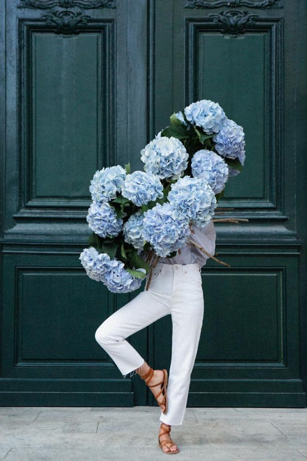 Centred In Self is a photo of a young girl in St Germain des Prés holding a giant bouquet of blue hydrangeas standing in a tree pose and is part of a limited edition series named Young Girl in Bloom by photographer Carla Coulson celebrating women loving and believing in themselves and building their self esteem by trusting their intuition.