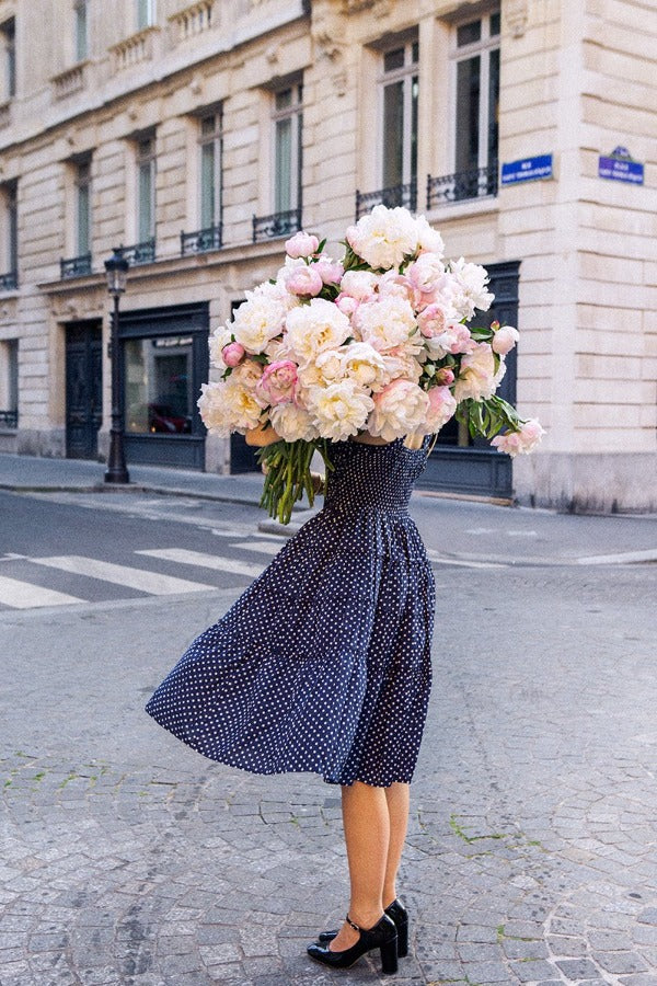 Standing Her Ground is a photo of a girl in Paris in St Germain des Prés holding the biggest bunch of ancient white peonies and is part of a limited edition series named Young Girl in Bloom by photographer Carla Coulson celebrating women loving and believing in themselves and building their self esteem by trusting their intuition.