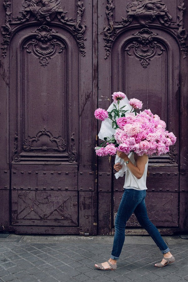 Girl On A Mission is a photo of a girl in St Germain des Prés in Paris with a big beautiful bouquet of pink peonies and is part of a limited edition series named Young Girl in Bloom by photographer Carla Coulson celebrating women loving and believing in themselves and building their self esteem by trusting their intuition.