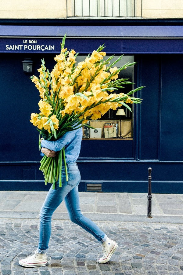 A Return to Love is a photo of a girl in Paris in St Germain des Prés with a huge bouquet of yellow gladiolus and is part of a limited edition series named Young Girl in Bloom by photographer Carla Coulson celebrating women loving and believing in themselves and building their self esteem by trusting their intuition.