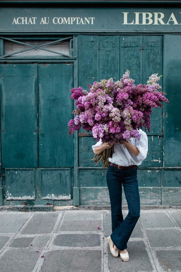 Beauty In Balance is a photo of a girl in St Germain des Prés holding a big bunch of lilacs and is part of a limited edition series named Young Girl in Bloom by photographer Carla Coulson celebrating women loving and believing in themselves and building their self esteem by trusting their intuition.