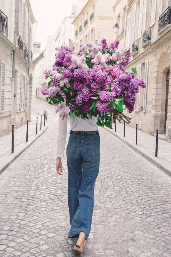 On My Way is a photo of a girl in Paris in St Germain des Prés holding a giant bouquet of lilacs and is part of a limited edition series named Young Girl in Bloom by photographer Carla Coulson celebrating women loving and believing in themselves and building their self esteem by trusting their intuition.