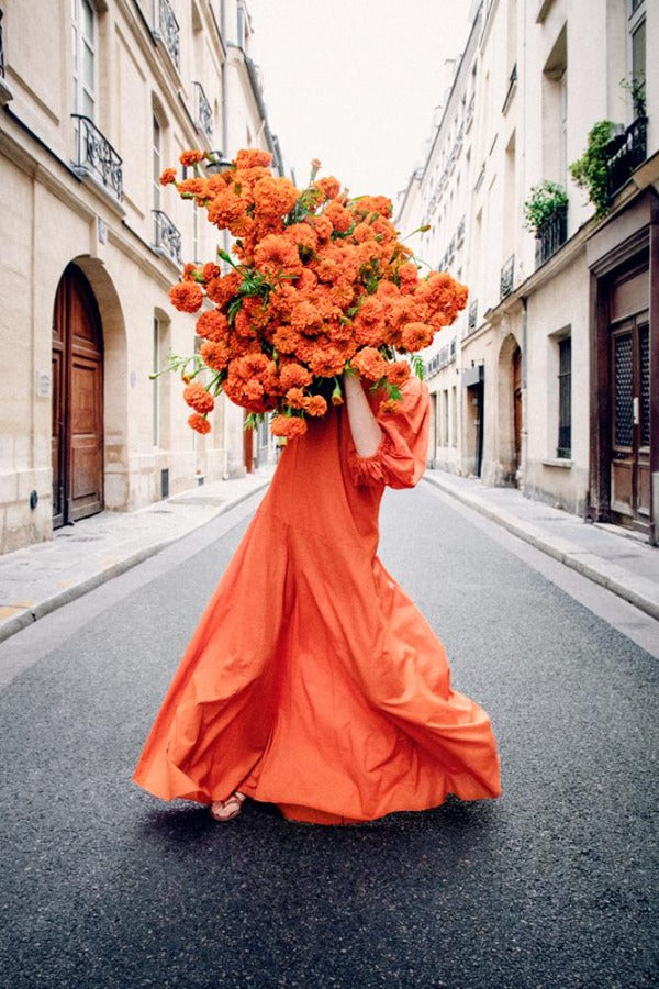 See Me is a photo of a girl in Paris holding a big bunch of orange flowers and is part of a limited edition series named Young Girl in Bloom by photographer Carla Coulson celebrating women loving and believing in themselves and building their self esteem by trusting their intuition.
