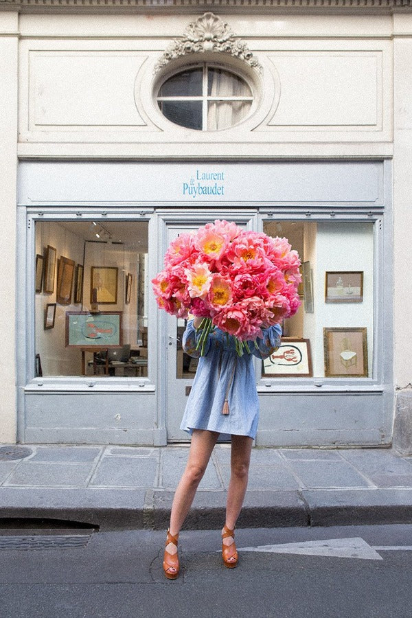 In Bloom is a photo of a girl in St Germain des Prés in Paris with a huge beautiful bunch of pink peonies and is part of a limited edition series named Young Girl in Bloom by photographer Carla Coulson celebrating women loving and believing in themselves and building their self esteem by trusting their intuition.